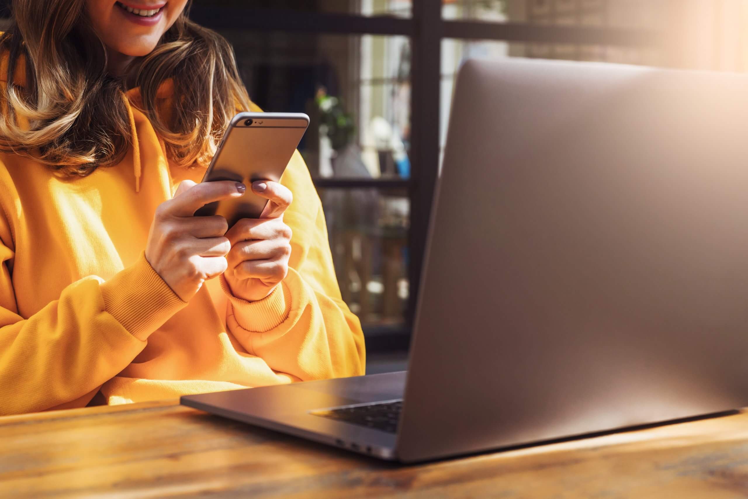 dziewczyna z żółtej bluzie ze smartfonem i laptopem
